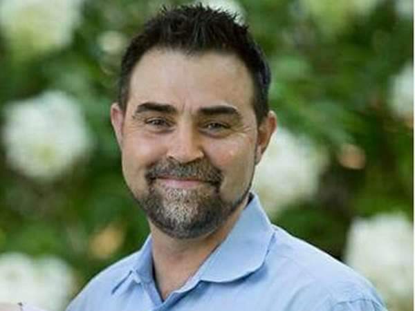 Photo of man (Adam Lovett) smiling, black hair and beard with blue shirt